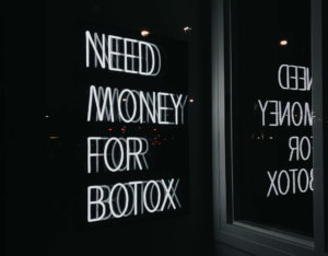 Light up sign in a window stating "need money for botox"